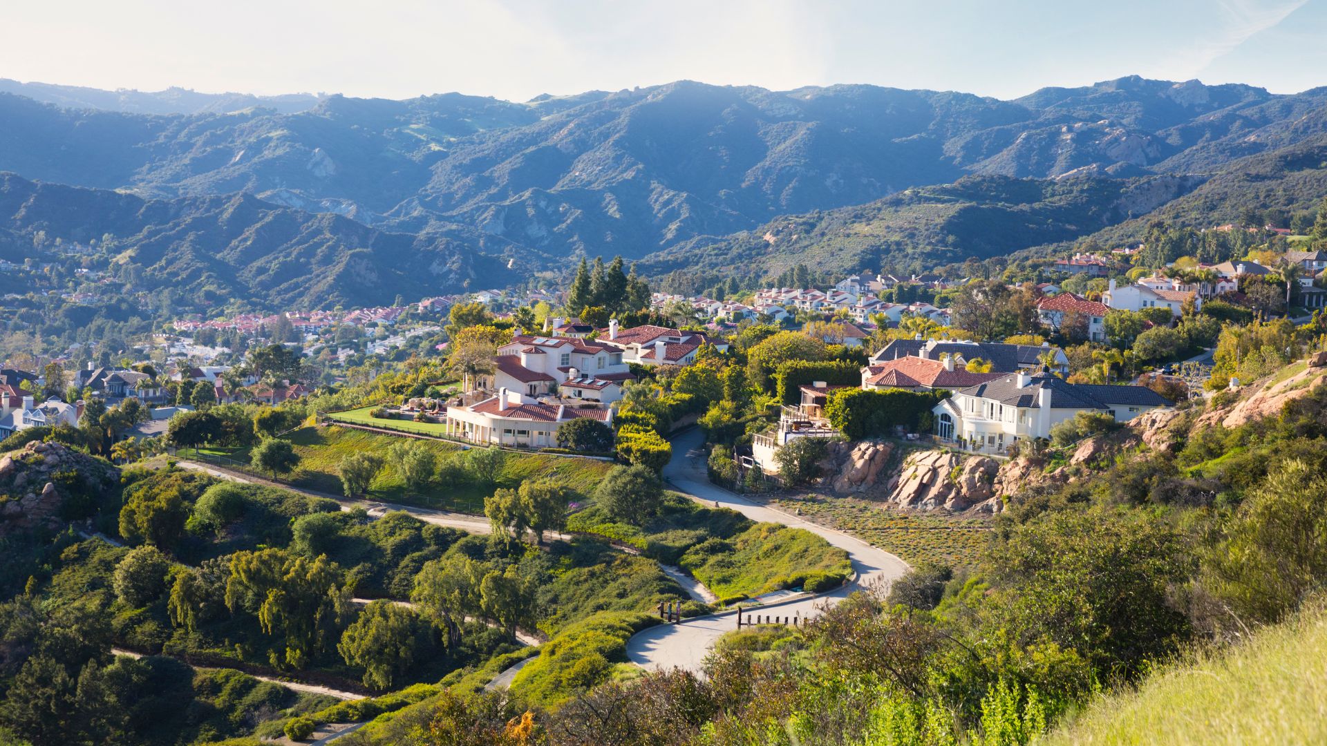 California hillside neighborhood with Spanish-style homes nestled against mountain ranges and brush-covered terrain